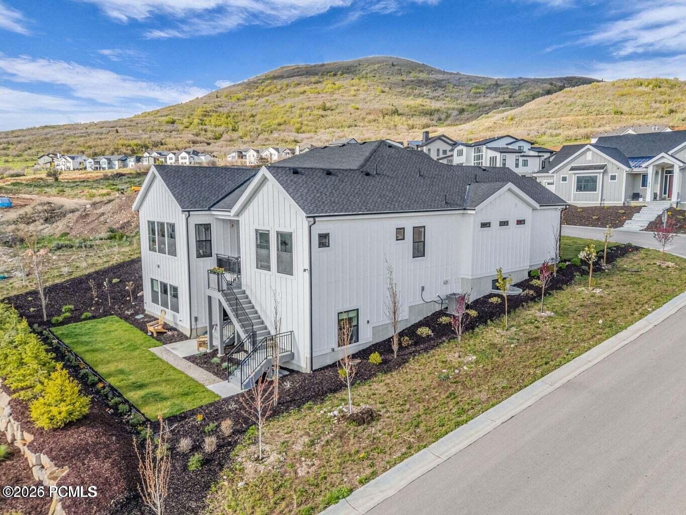 View of side of home with a yard, roof with shingles, a mountain view, and board and batten siding