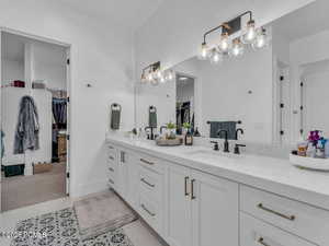 Full bath with a walk in closet, double vanity, and light tile patterned floors