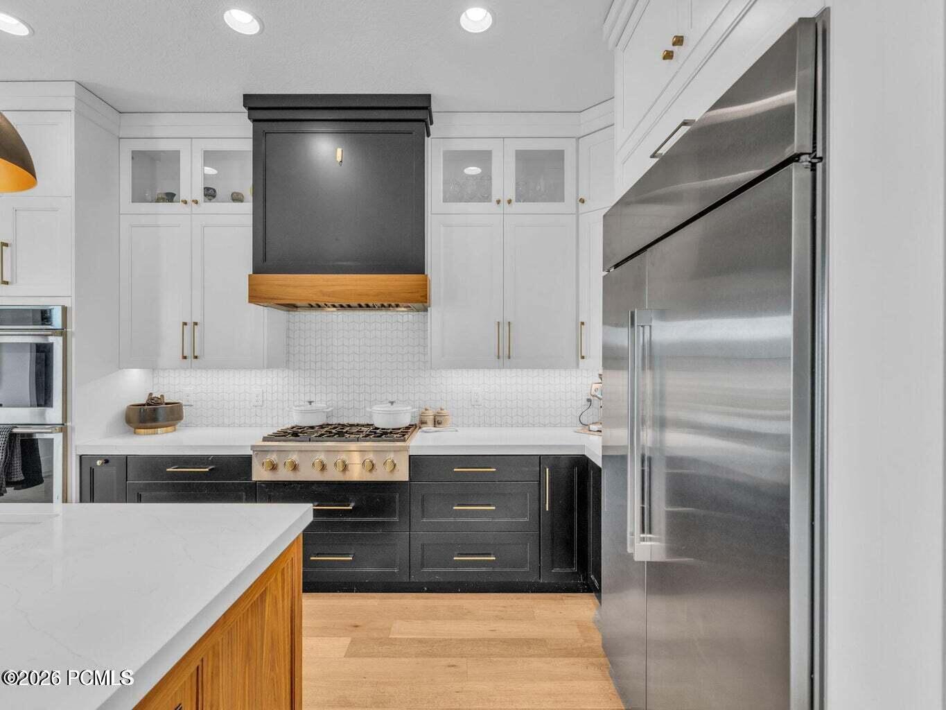 Kitchen with two tone cabinetry, stainless steel appliances, light wood-style flooring, light stone countertops, and recessed lighting