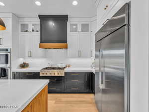 Kitchen with two tone cabinetry, stainless steel appliances, light wood-style flooring, light stone countertops, and recessed lighting