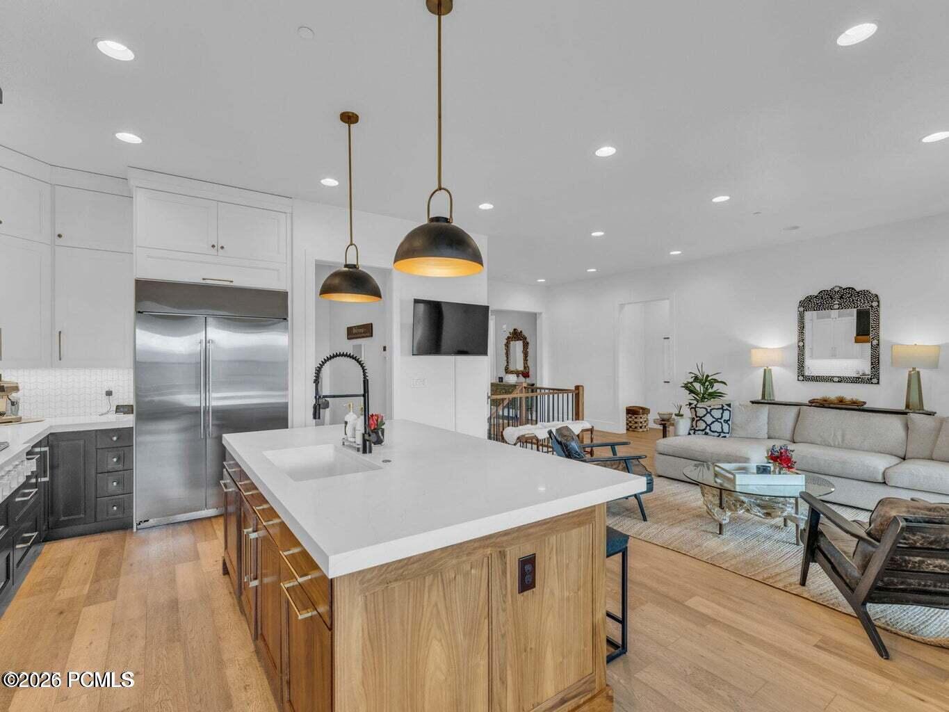 Dual tone kitchen featuring dual tone cabinets, open floor plan, hanging light fixtures, built in refrigerator, and an island with sink