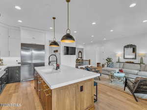 Dual tone kitchen featuring dual tone cabinets, open floor plan, hanging light fixtures, built in refrigerator, and an island with sink