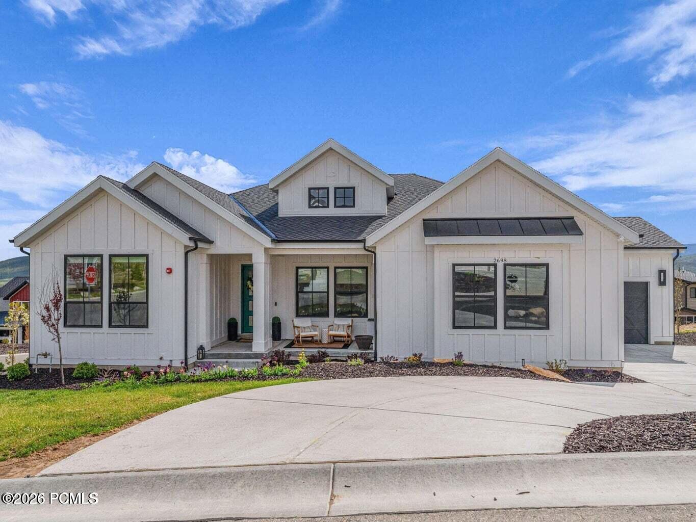 Modern farmhouse style home with roof with shingles, board and batten siding, a porch, and driveway