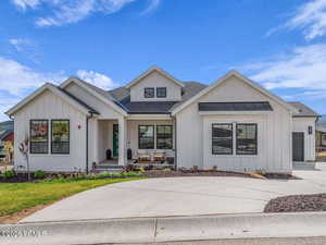Modern farmhouse style home with roof with shingles, board and batten siding, a porch, and driveway
