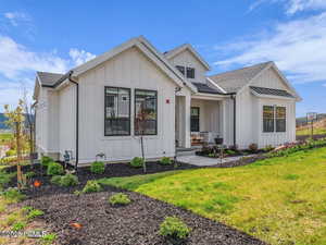 Back of house with board and batten siding, a shingled roof, and a yard