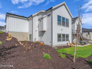 Rear view of house with board and batten siding, a balcony, and a lawn