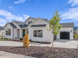 Modern farmhouse style home featuring board and batten siding, a shingled roof, a standing seam roof, and a garage