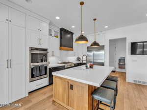Two tone kitchen featuring dual tone cabinetry, an island with sink, stainless steel appliances, light wood-style floors, and a breakfast bar area
