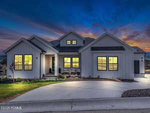 Modern farmhouse with board and batten siding, a shingled roof, driveway, and covered porch