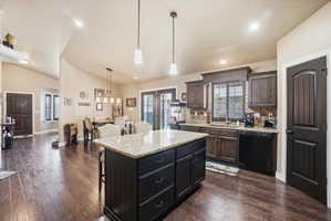 Kitchen featuring a breakfast bar, light stone counters, a kitchen island, dishwasher, and vaulted ceiling