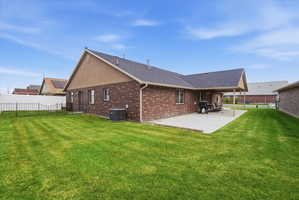Rear view of house featuring a fenced backyard, brick siding, a shingled roof, and a patio area
