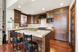 Kitchen featuring light countertops, built in appliances, a kitchen breakfast bar, glass fronted cabinets, and recessed lighting
