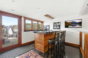 Indoor dry bar featuring dark countertops, dark tile patterned flooring, and wood finish cabinetry
