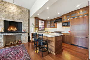 Kitchen featuring dark wood-style floors, built in appliances, glass fronted cabinets, a center island, and wood finish cabinets