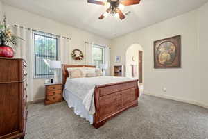Bedroom featuring ceiling fan, carpet floors, arched walkways, and ensuite bath