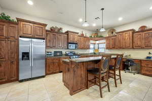 Kitchen featuring a kitchen bar, stainless steel appliances, dark stone countertops, a kitchen island, and pendant lighting