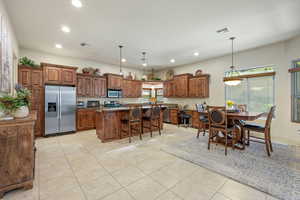 Kitchen featuring a breakfast bar, wood finish cabinetry, stainless steel appliances, a center island, and light tile patterned floors