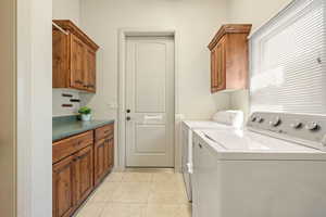Laundry room featuring cabinet space, light tile patterned floors, and washing machine and dryer