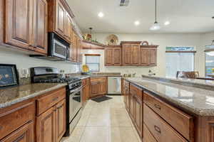 Kitchen featuring stainless steel appliances, dark stone counters, pendant lighting, and wood finish cabinets