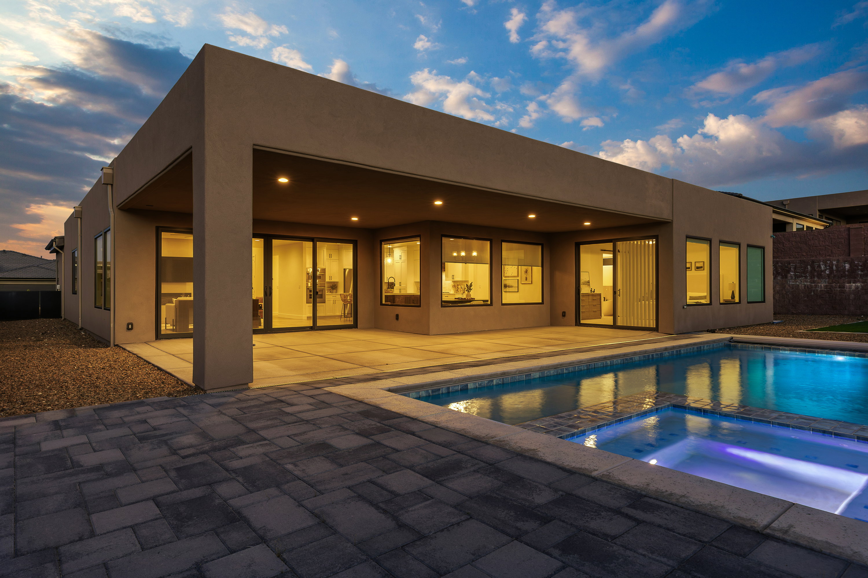 Back of property at dusk with a patio, a pool with connected hot tub, and stucco siding