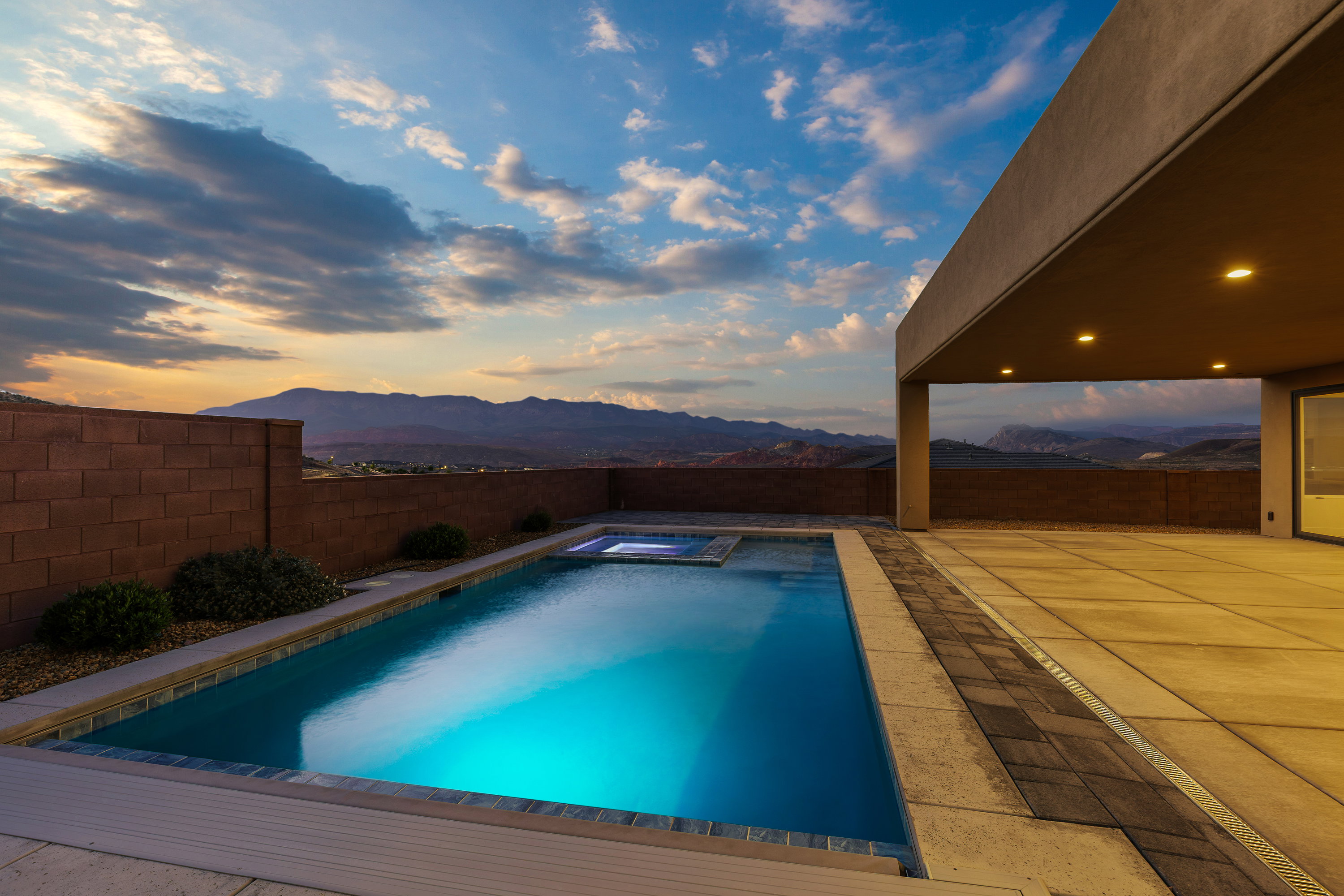 Pool at dusk featuring a mountain view, a patio, a fenced backyard, and a pool with connected hot tub