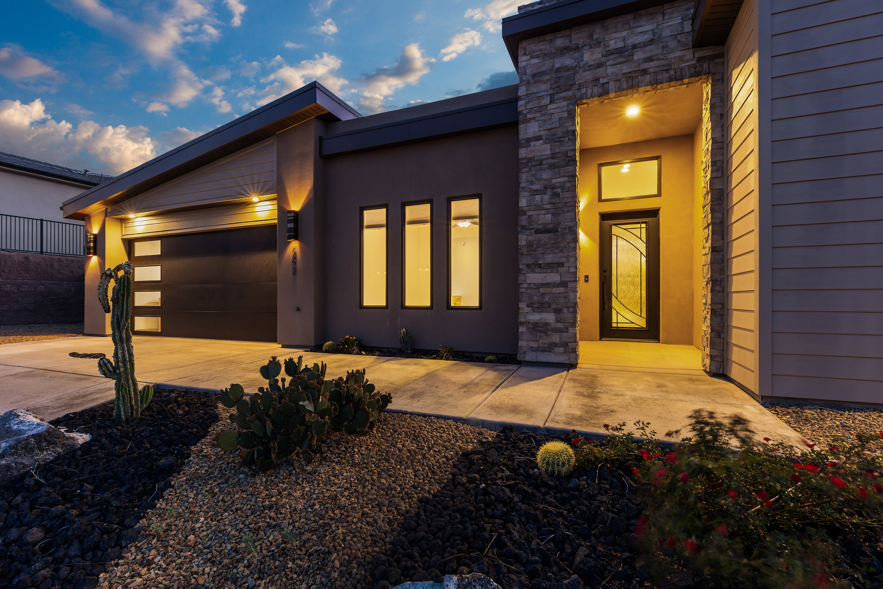 View of front of home with an attached garage, stone siding, driveway, and stucco siding