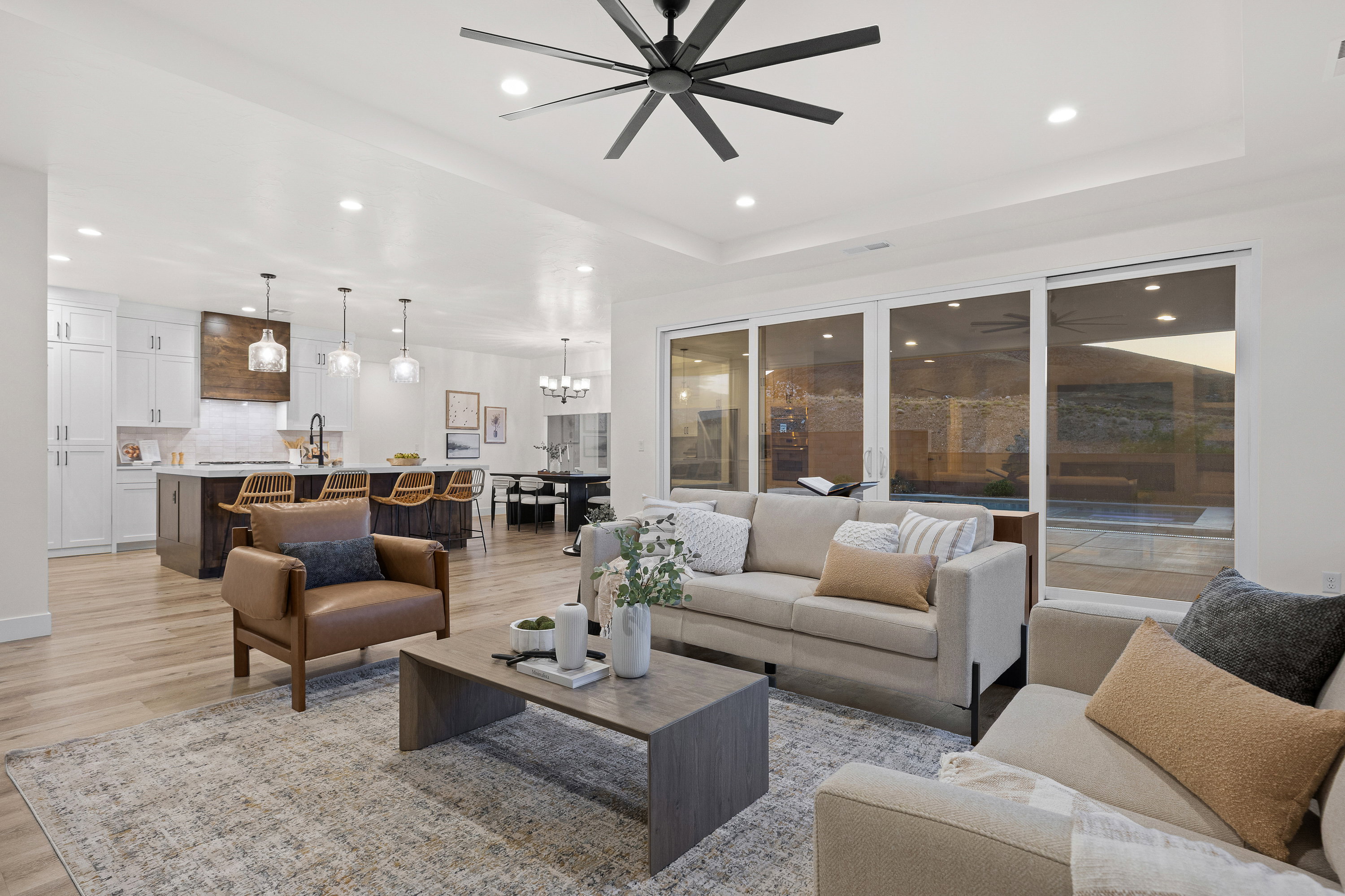 Living area with light wood-style floors, suspended lighting, ceiling fan, and a tray ceiling