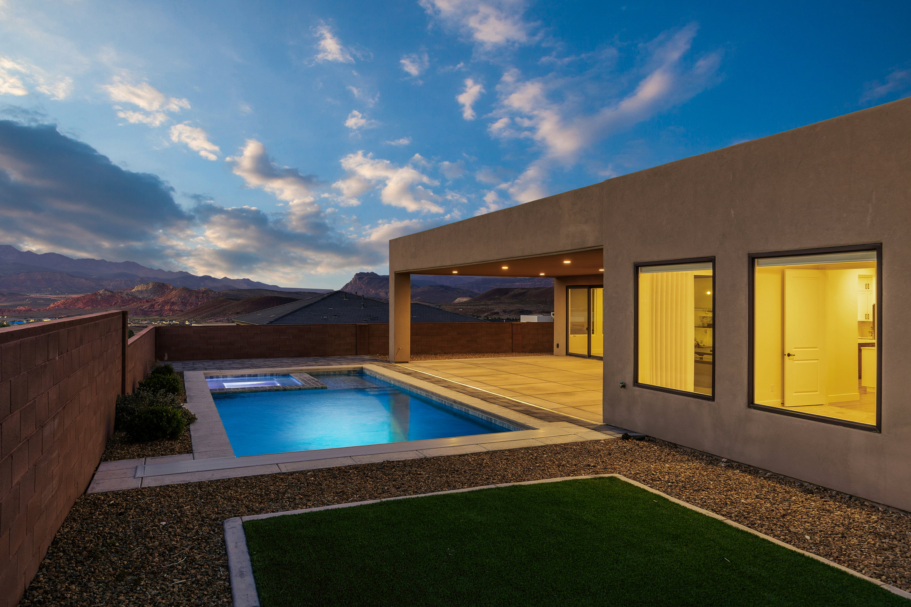 Pool at dusk with a patio area, a mountain view, a fenced backyard, and a pool with connected hot tub