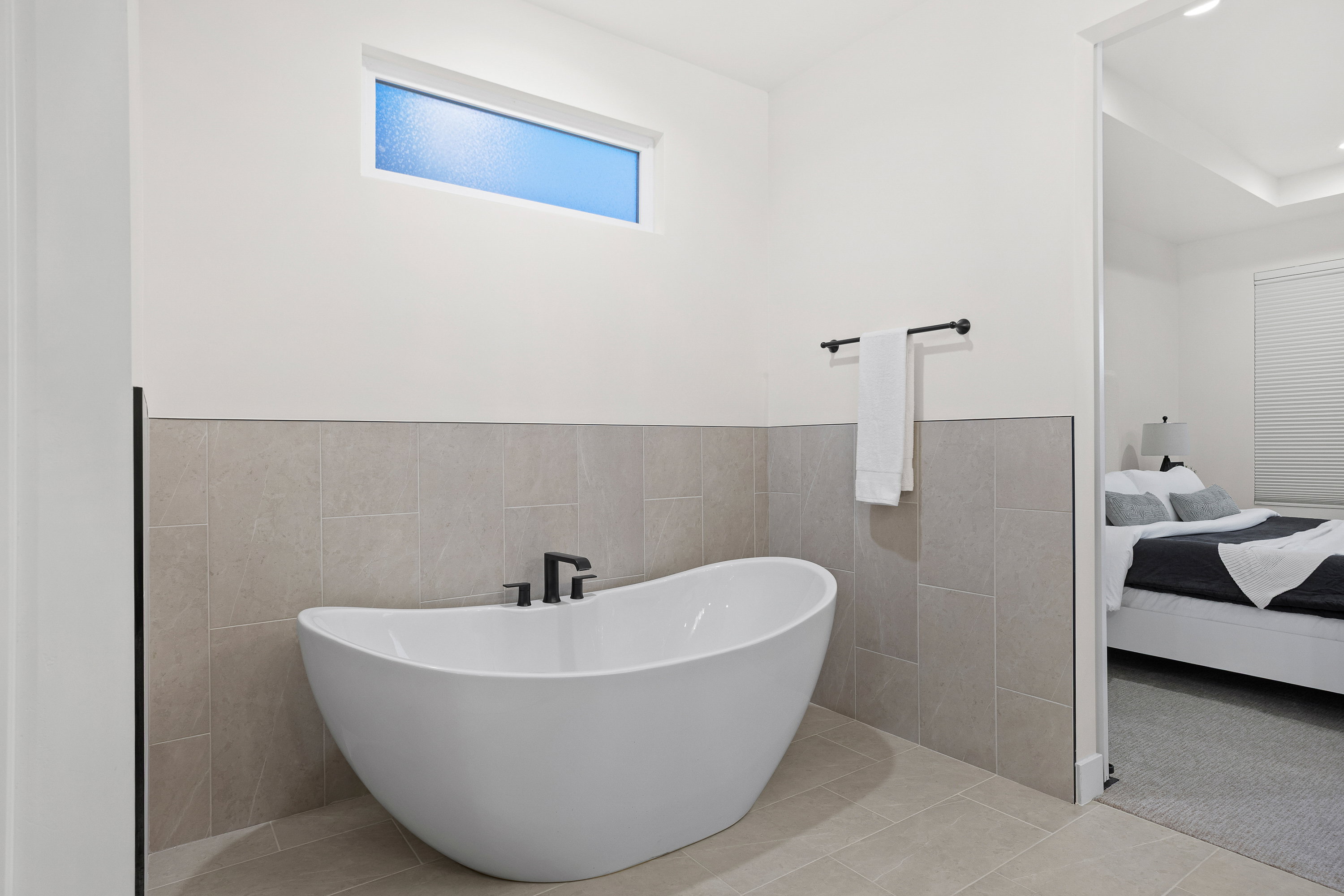 Ensuite bathroom with tile walls, a freestanding tub, light tile patterned floors, and a wainscoted wall