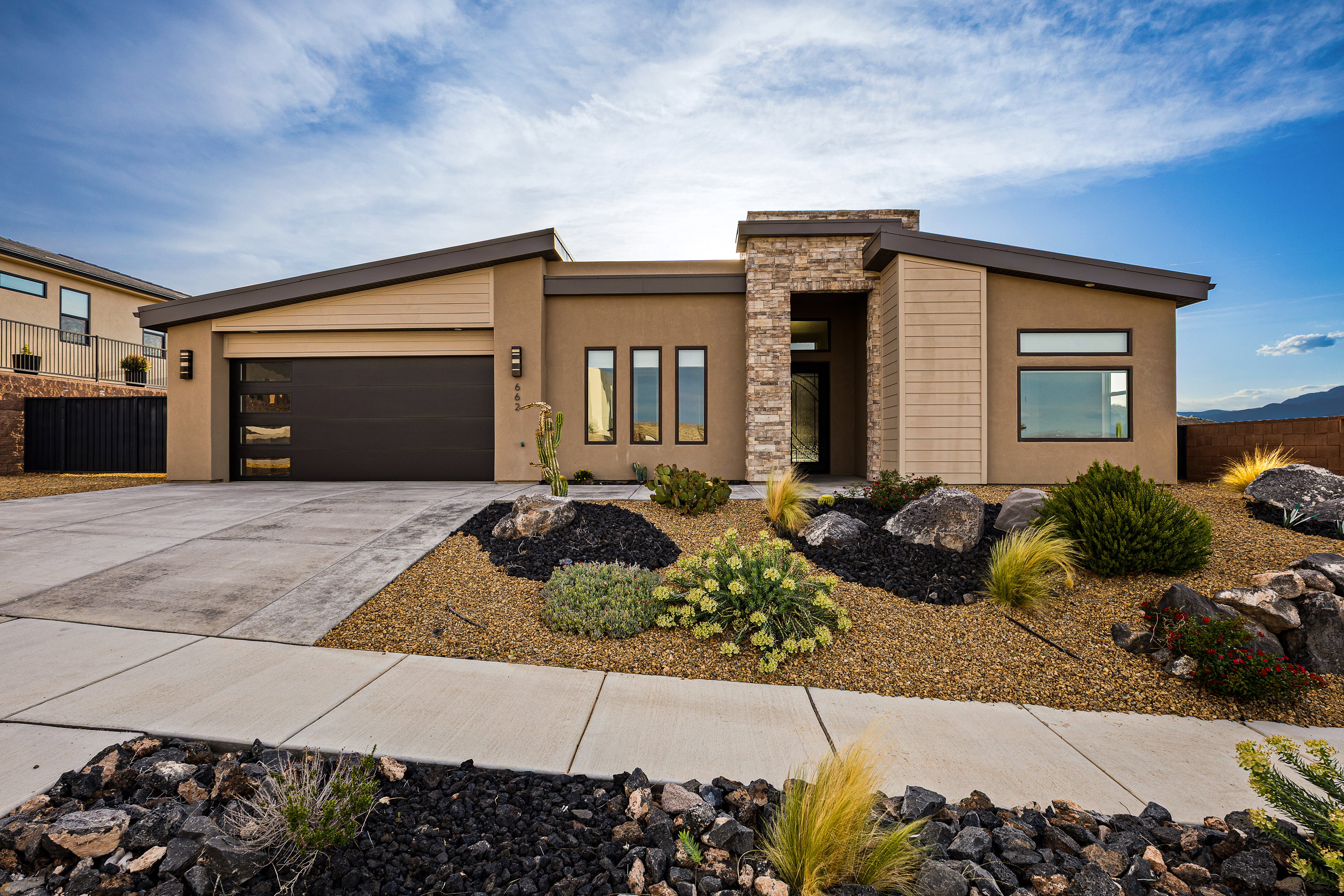 Contemporary house with an attached garage, driveway, stone siding, and stucco siding