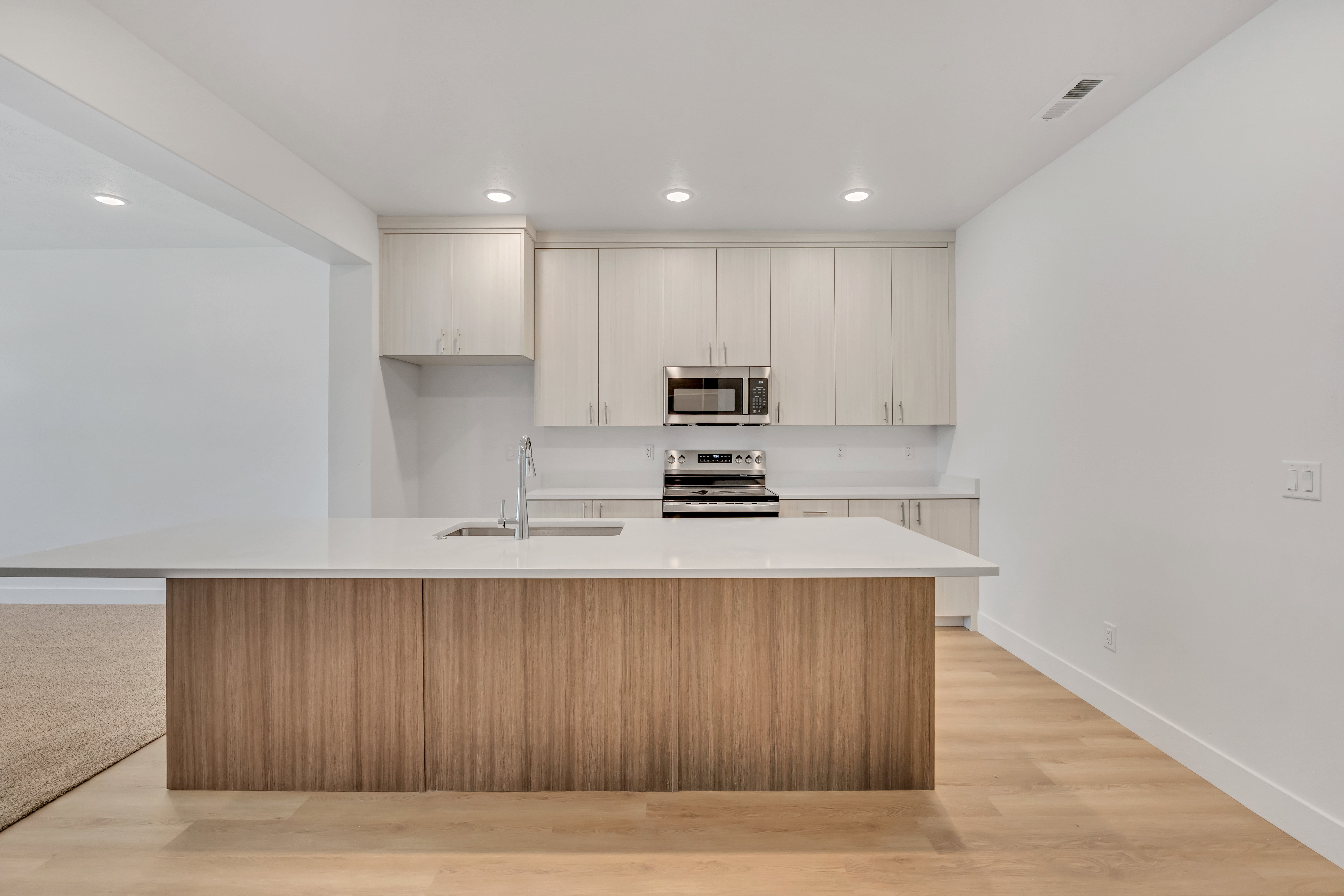 Kitchen featuring a large central island with a light wood-finish base and a light-toned countertop, stainless steel appliances, upper and lower cabinetry, and recessed lighting