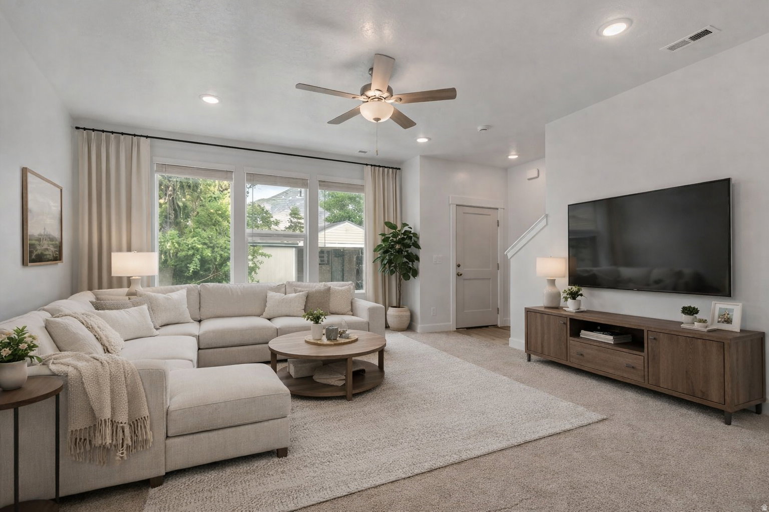 Bright living area featuring recessed lighting, a ceiling fan, large windows with neutral curtains, and light-colored carpeting