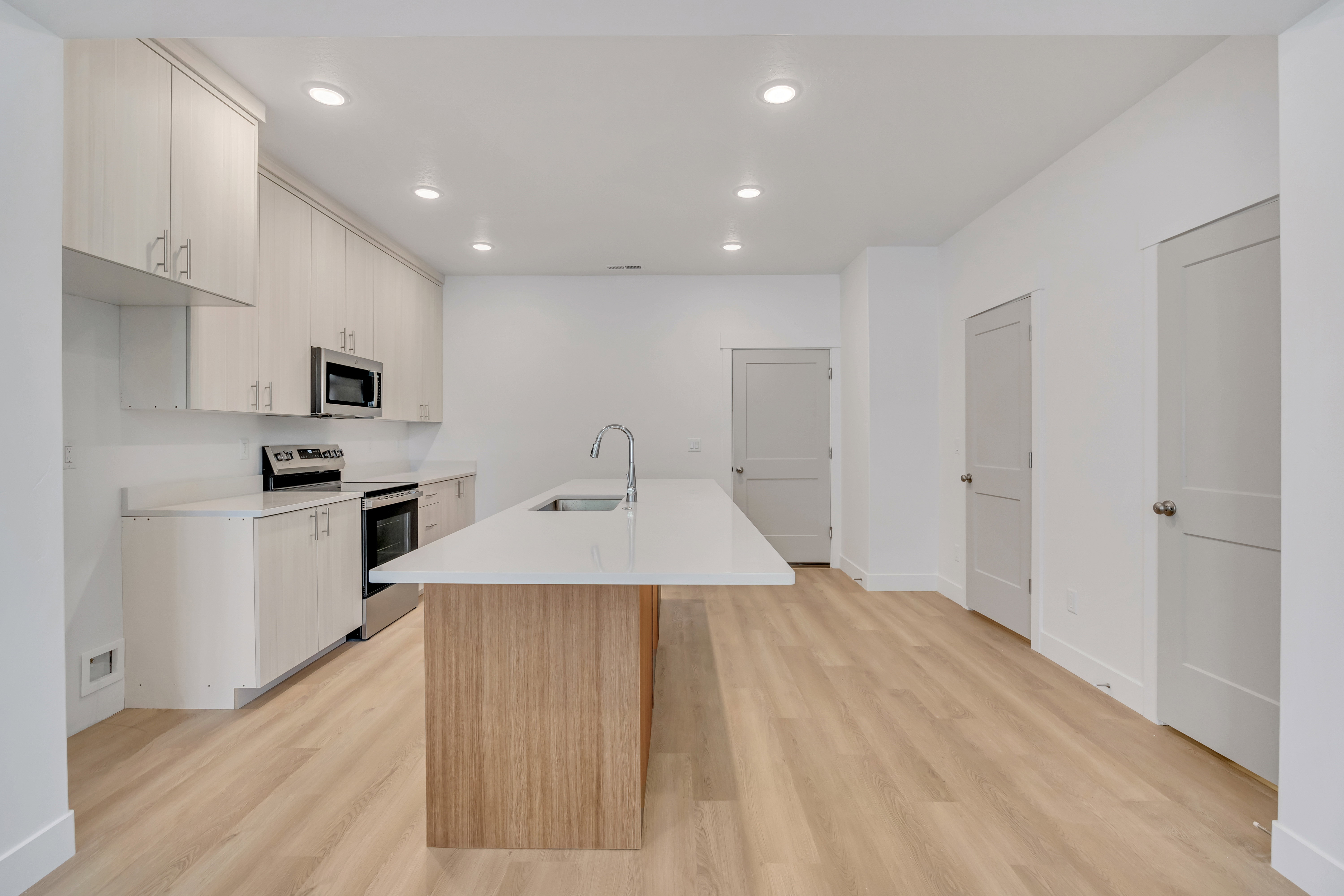 Contemporary kitchen featuring light wood-finish cabinetry, stainless steel appliances, a white countertop, and a large center island with an undermount sink