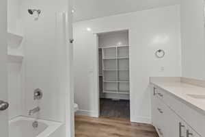 Bathroom with vanity, light wood-style floors, a spacious closet, and bathing tub / shower combination