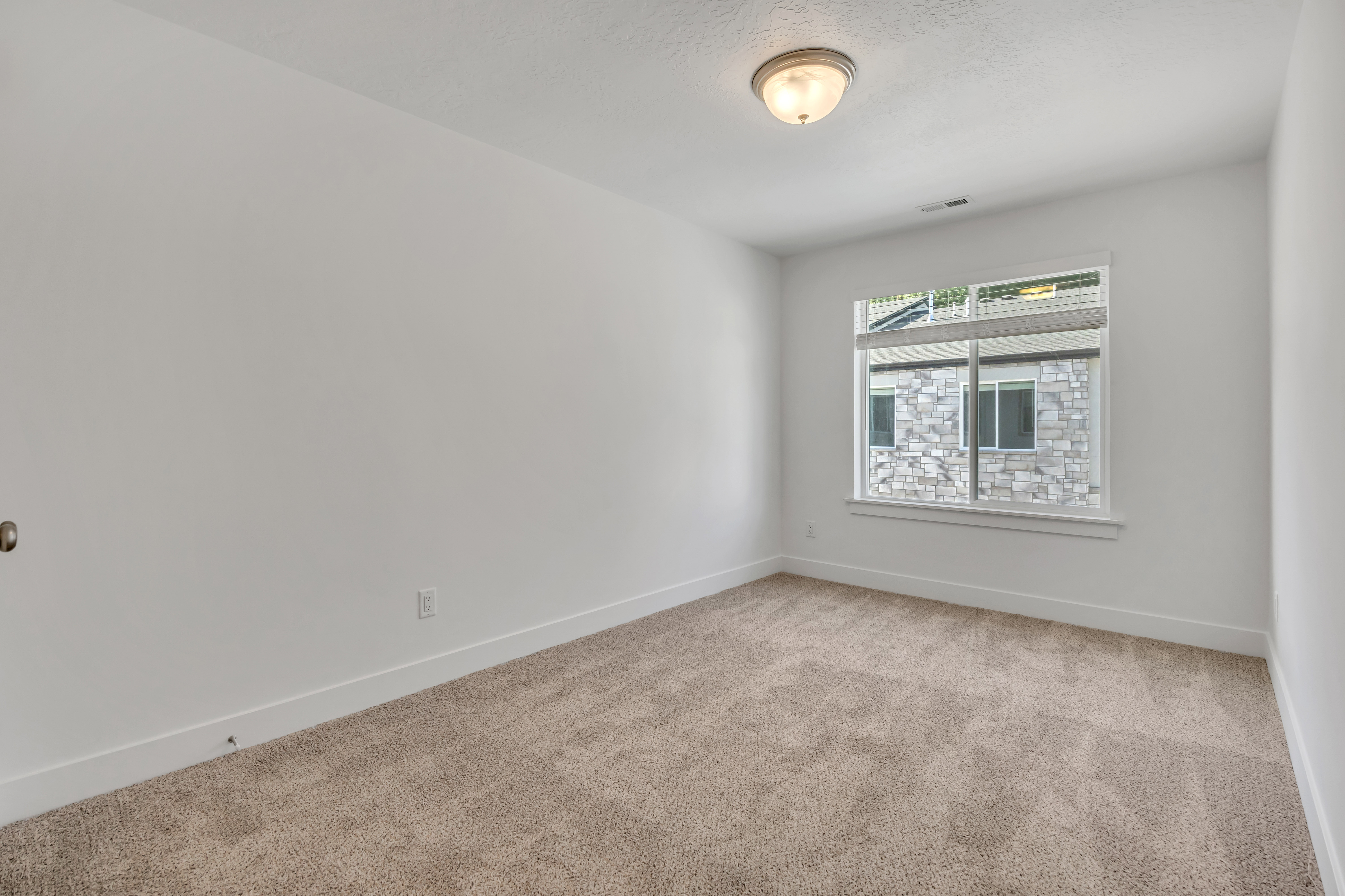 Neutral tone carpeted room featuring white walls, a large window with blinds, and a flush mount ceiling light fixture