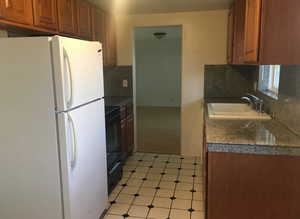 Kitchen with freestanding refrigerator, tile counters, black electric range, tasteful backsplash, and light floors