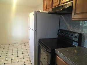 Kitchen featuring black electric range oven, tile countertops, wood finish cabinets, and light flooring