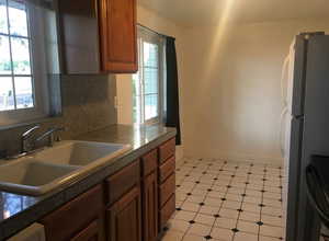 Kitchen featuring tile counters, tasteful backsplash, black stove, wood finish cabinetry, and freestanding refrigerator