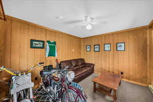 Carpeted living room with a ceiling fan and wooden walls