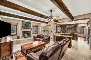 Living area with beamed ceiling, a glass covered fireplace, stone tile floors, and ceiling fan