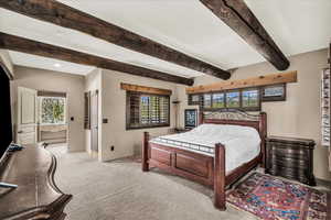 Bedroom featuring light colored carpet, multiple windows, and beamed ceiling