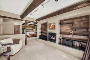 Carpeted living area with track lighting, a glass covered fireplace, and beam ceiling