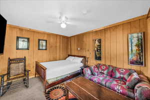 Carpeted bedroom with a ceiling fan and wood walls