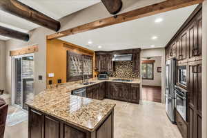 Kitchen featuring dark wood finish cabinetry, stone tile flooring, a peninsula, light stone countertops, and recessed lighting