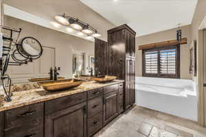 Bathroom with double vanity, stone tile floors, and a garden tub
