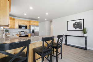 Kitchen featuring light wood finish cabinets, a kitchen breakfast bar, stainless steel appliances, dark stone countertops, and light wood-style flooring