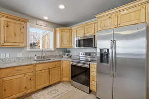 Kitchen with stainless steel appliances, light wood finish cabinetry, light stone countertops, and recessed lighting
