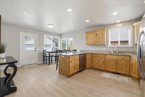 Kitchen with a peninsula, light stone countertops, light wood-style flooring, stainless steel appliances, and recessed lighting