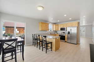 Kitchen featuring light wood finish cabinets, stainless steel appliances, a peninsula, light wood-style flooring, and plenty of natural light