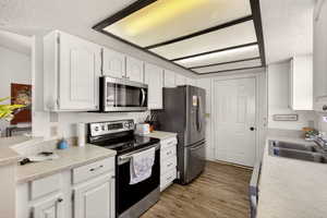 Kitchen with stainless steel appliances, a textured ceiling, white cabinets, light countertops, and dark wood-style floors